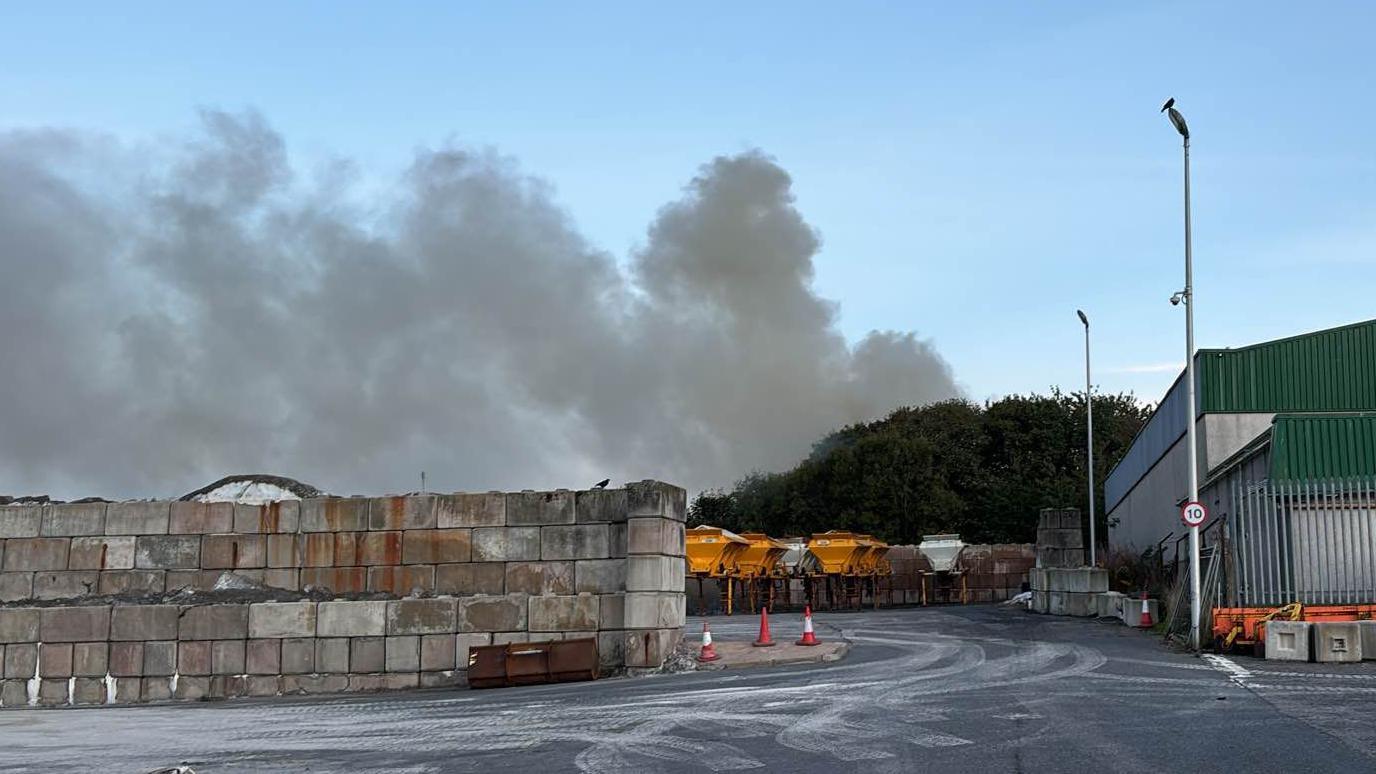 clouds of smoke above trees behind an empty car park