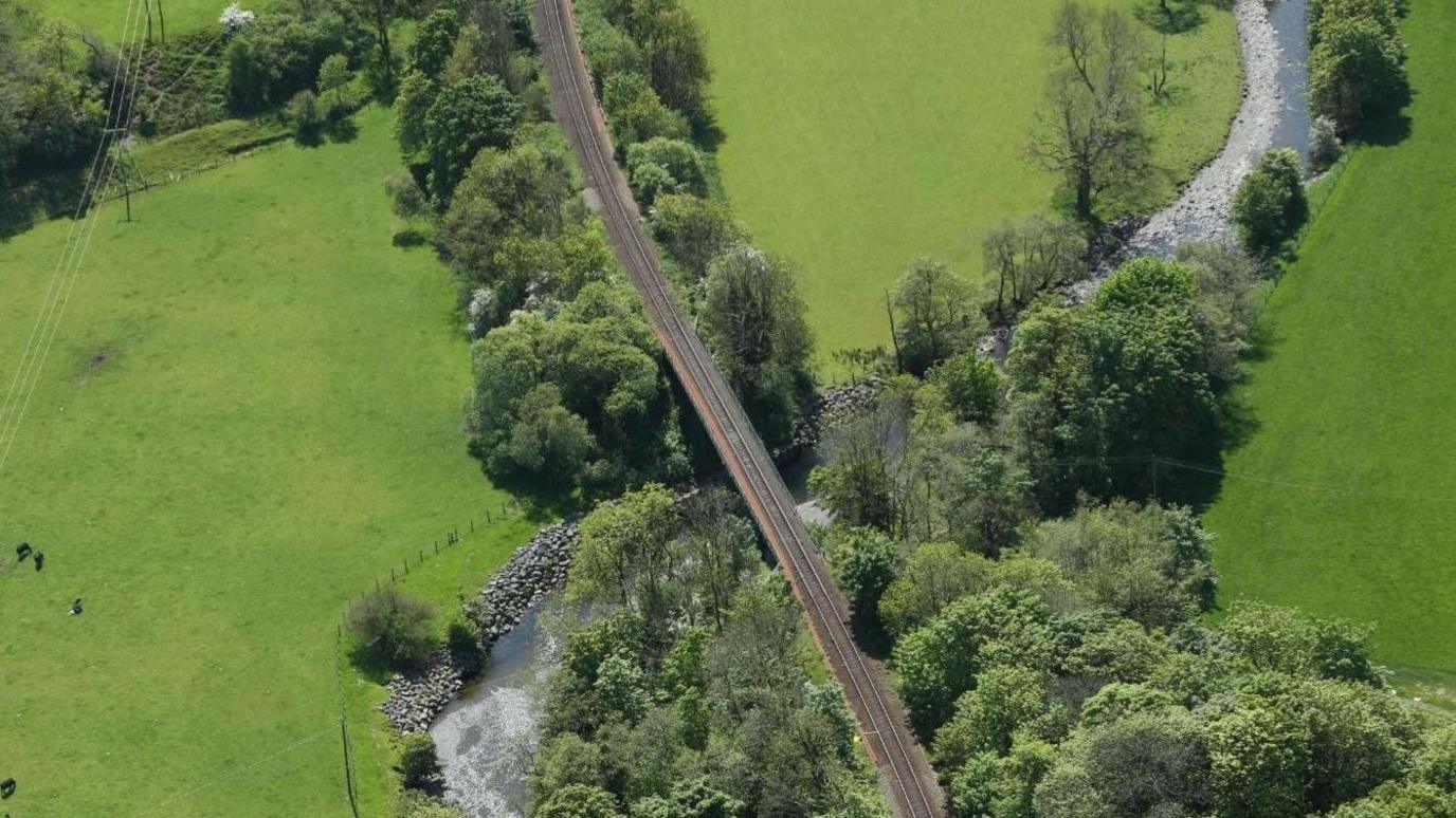 Rural rail track including bridge crossing over river.
