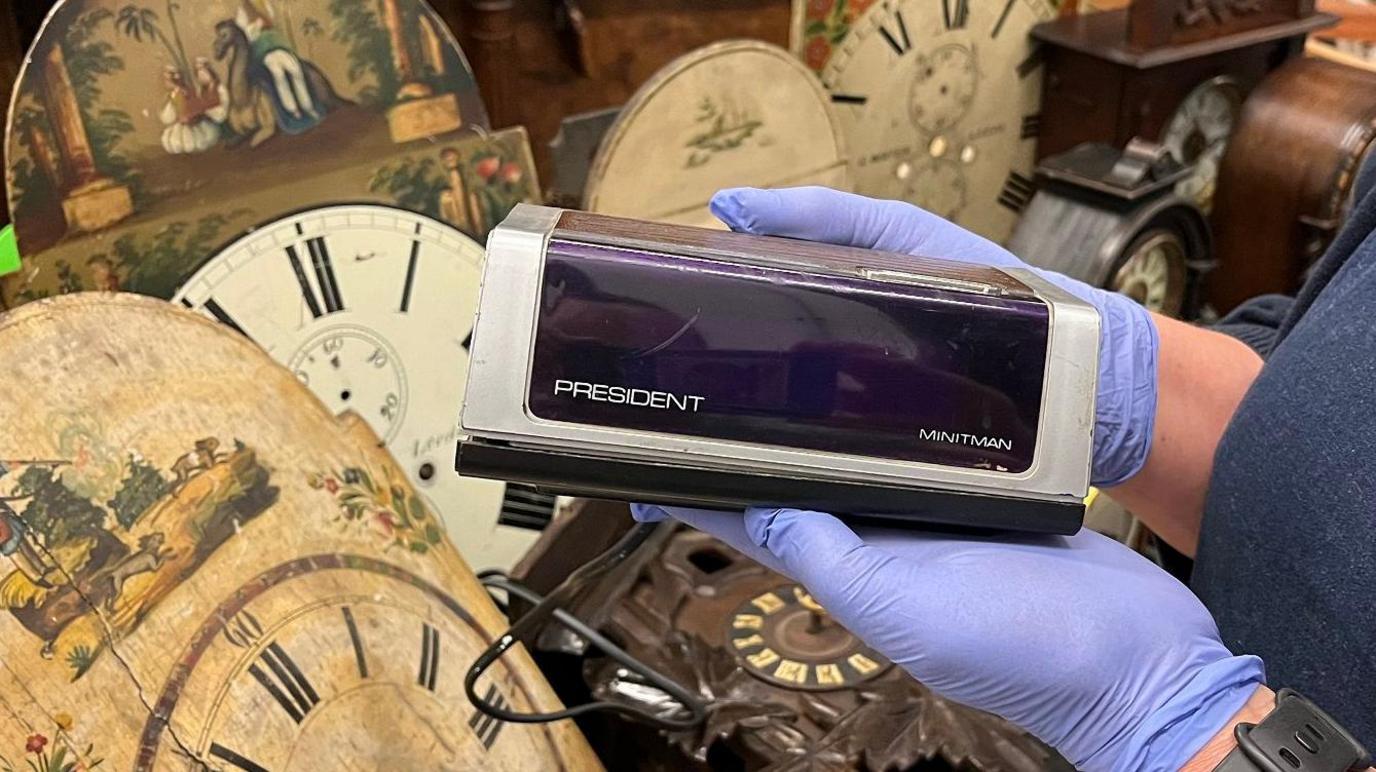 A 1970s digital clock being held by a woman with blue gloves