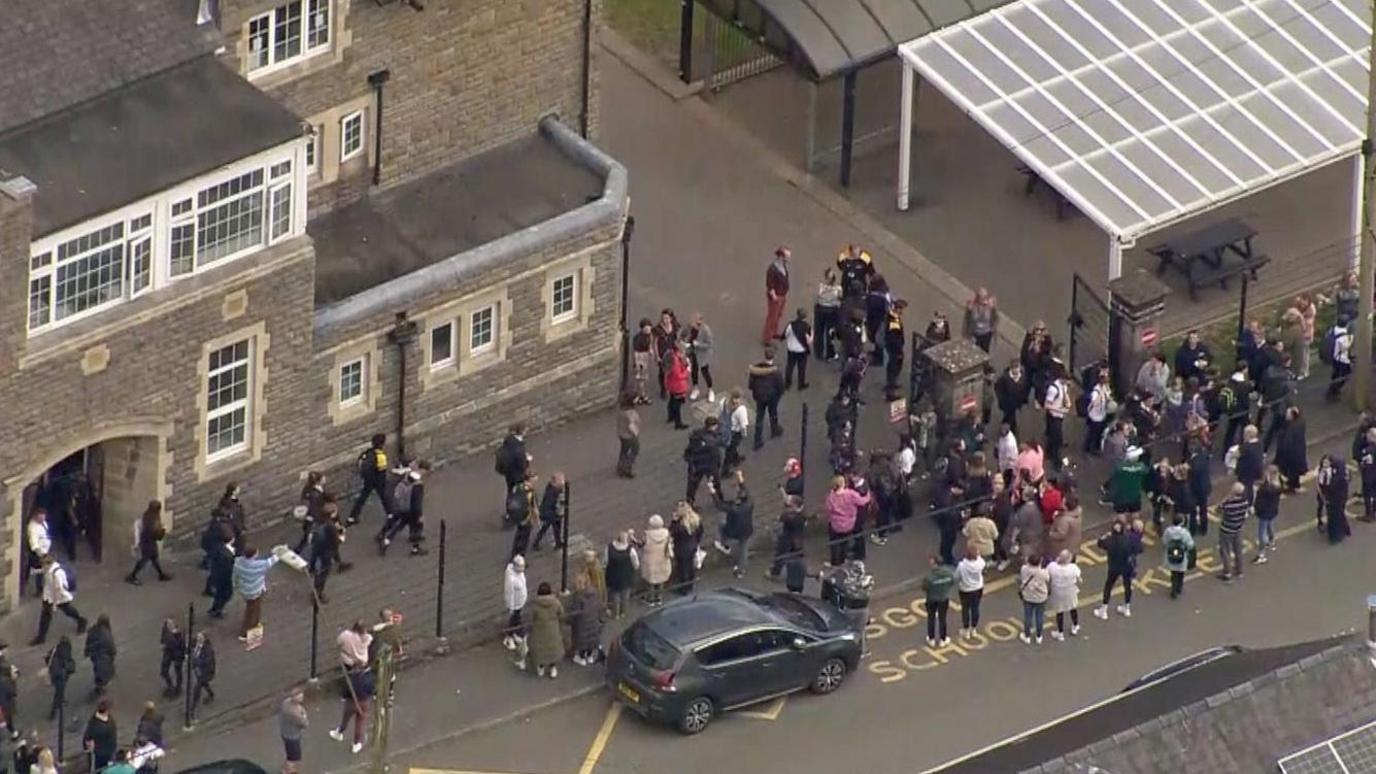 Crowds of parents lined up outside Ysgol Dyffryn Aman seen from a drone above
