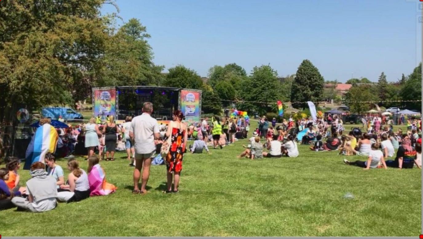 People in a field - mostly sitting - watching entertainment on a stage