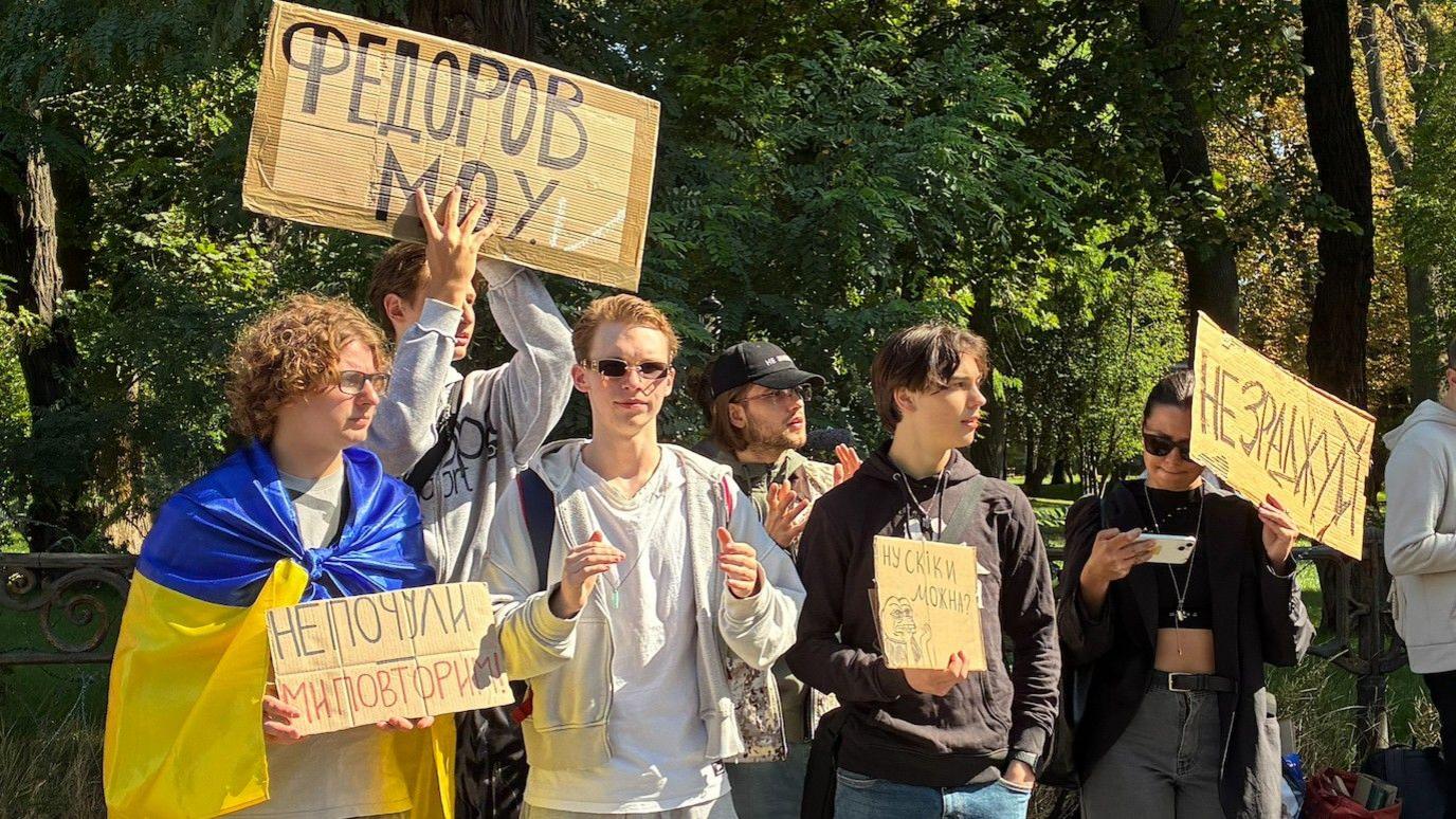Young people hold up placards including one draped in a yellow and blue Ukrainian flag