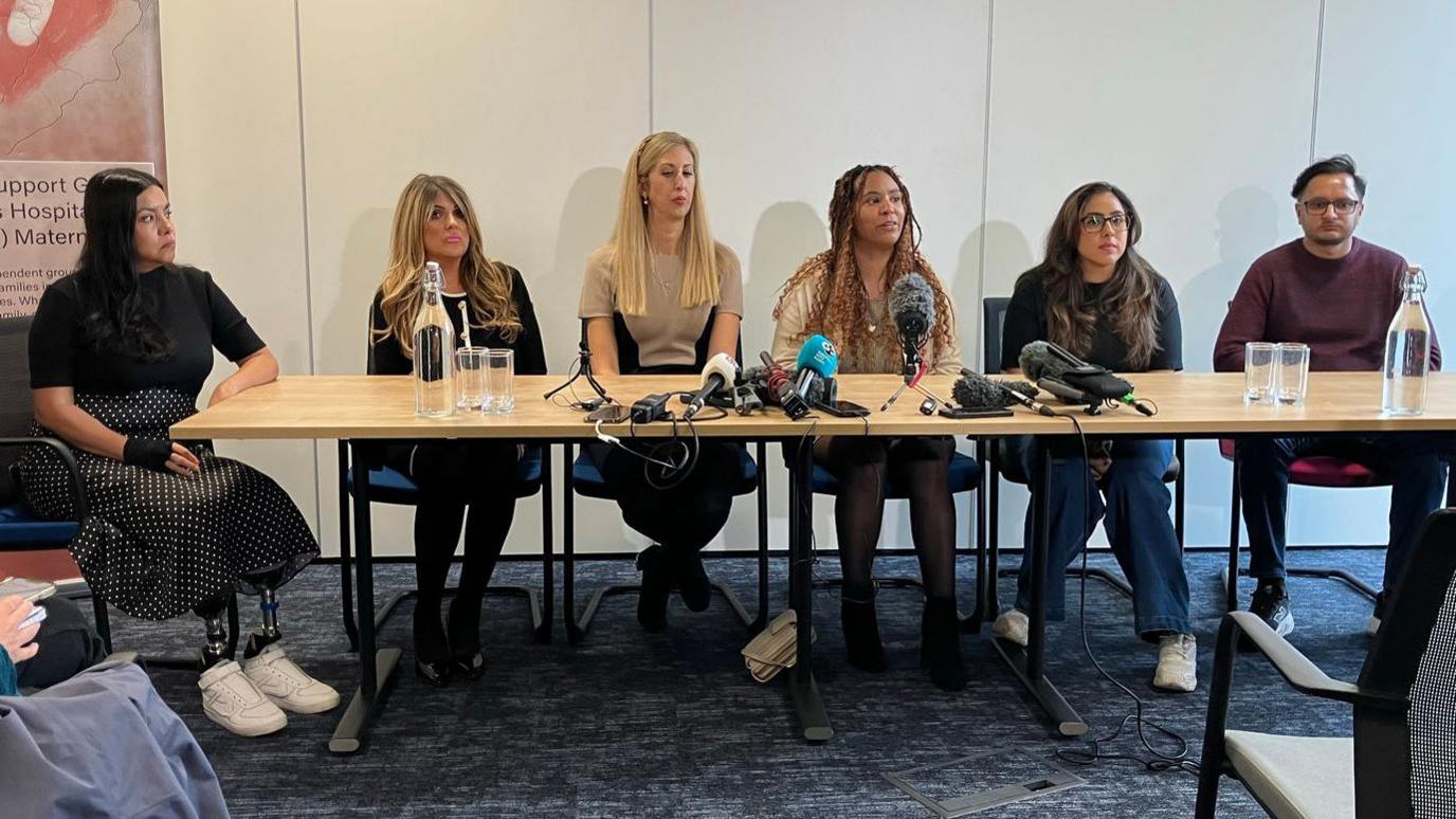 Five women and a man sit at a table, all facing forwards.