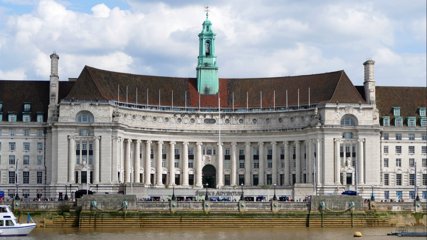 Front of London County Hall, a large building with columns with the River Thames running in front of it