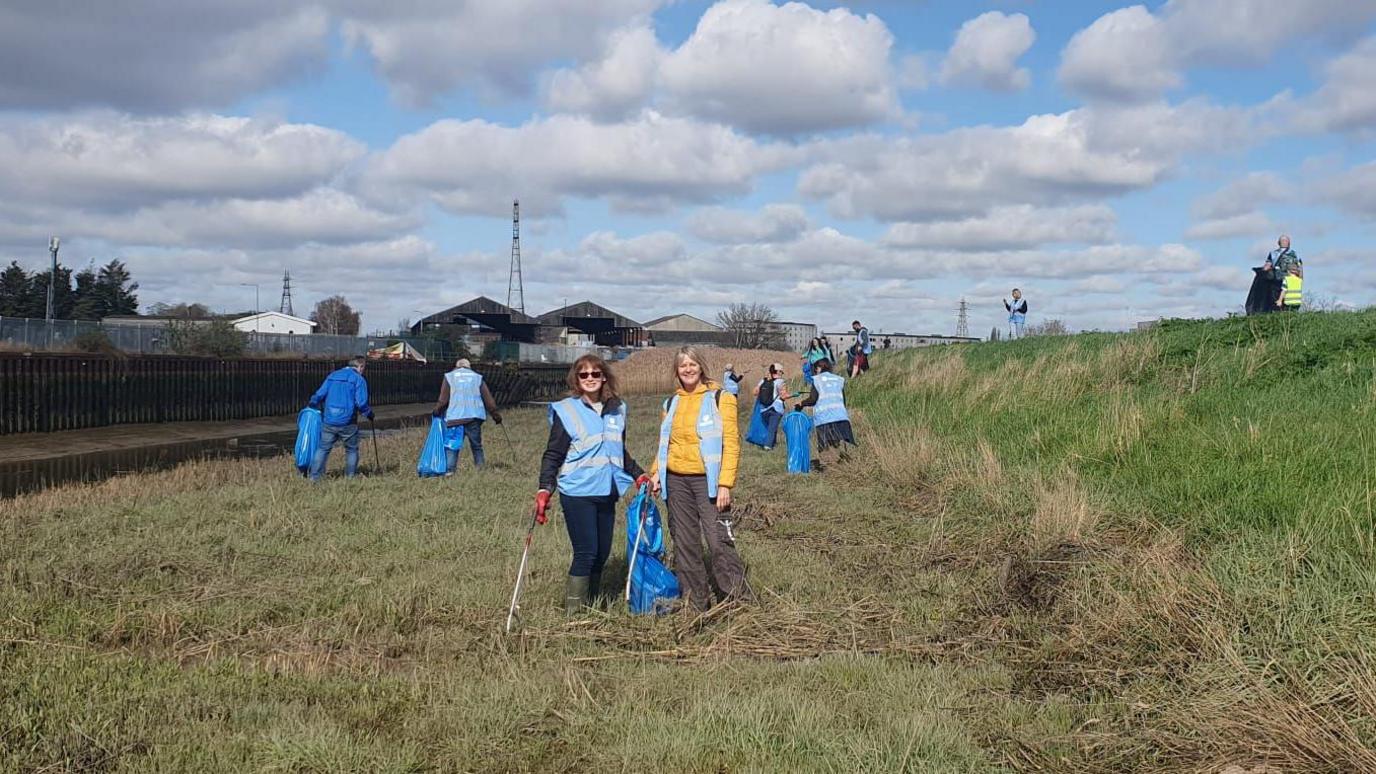 People holding blue bags and litter-pickers on the grass next to the River Colne in Colchester.