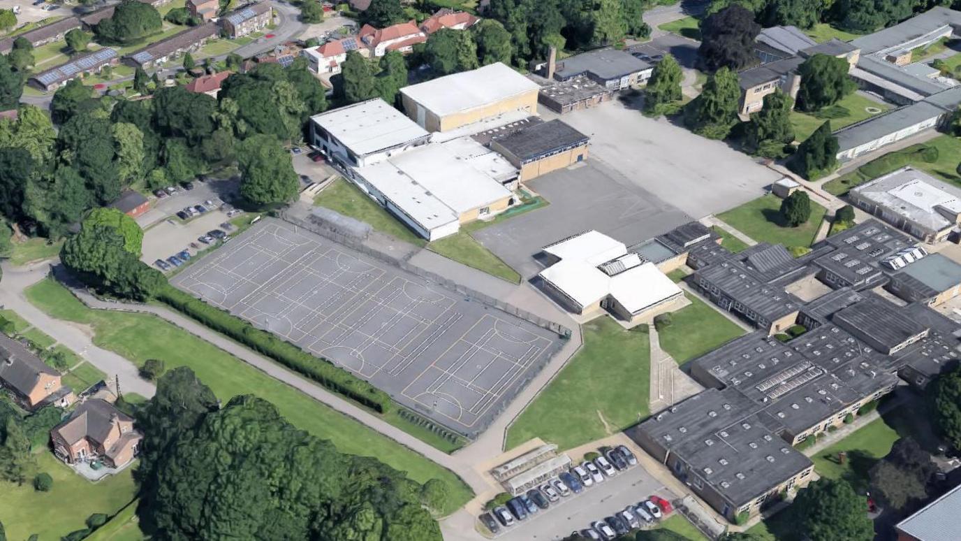 An aerial view of ELA Active Impington, showing the whole sports centre site, including netball courts at the centre of the plans, along with other buildings on the site, surrounded by trees and residential properties