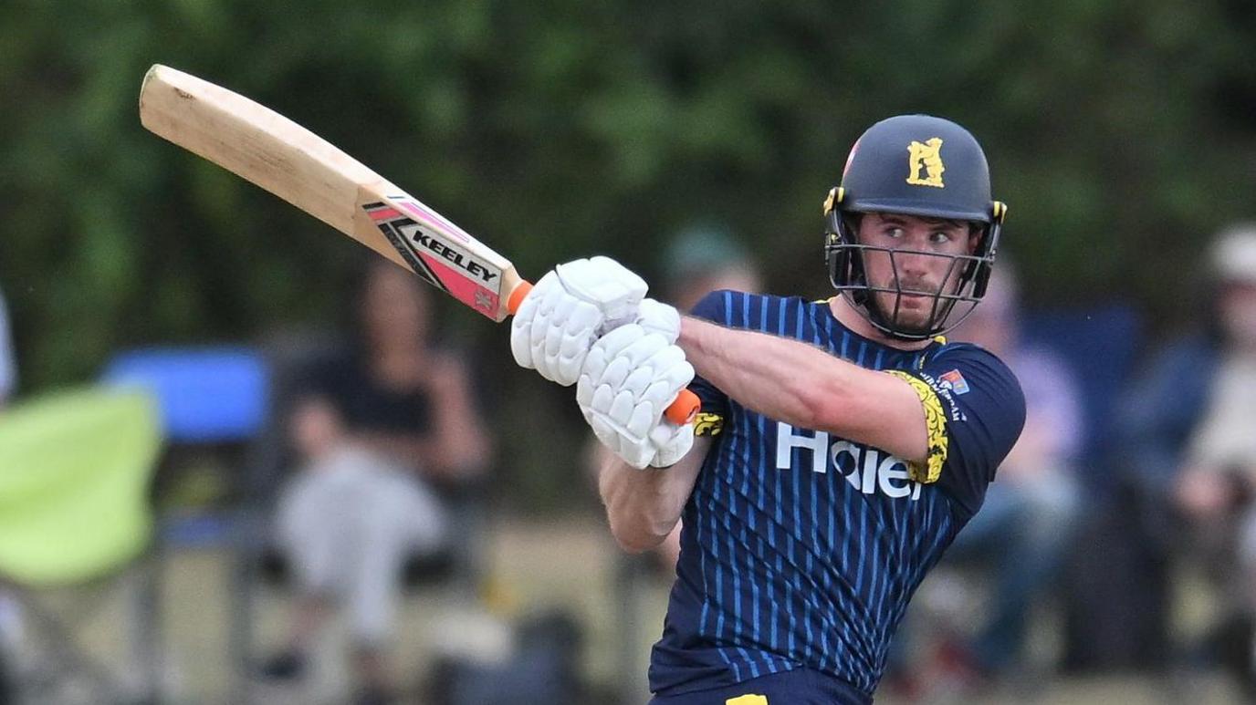 Warwickshire's George Garton, wearing a navy blue helmet and navy blue kit with lighter blue pinstripes on the chest, plays a hook shot