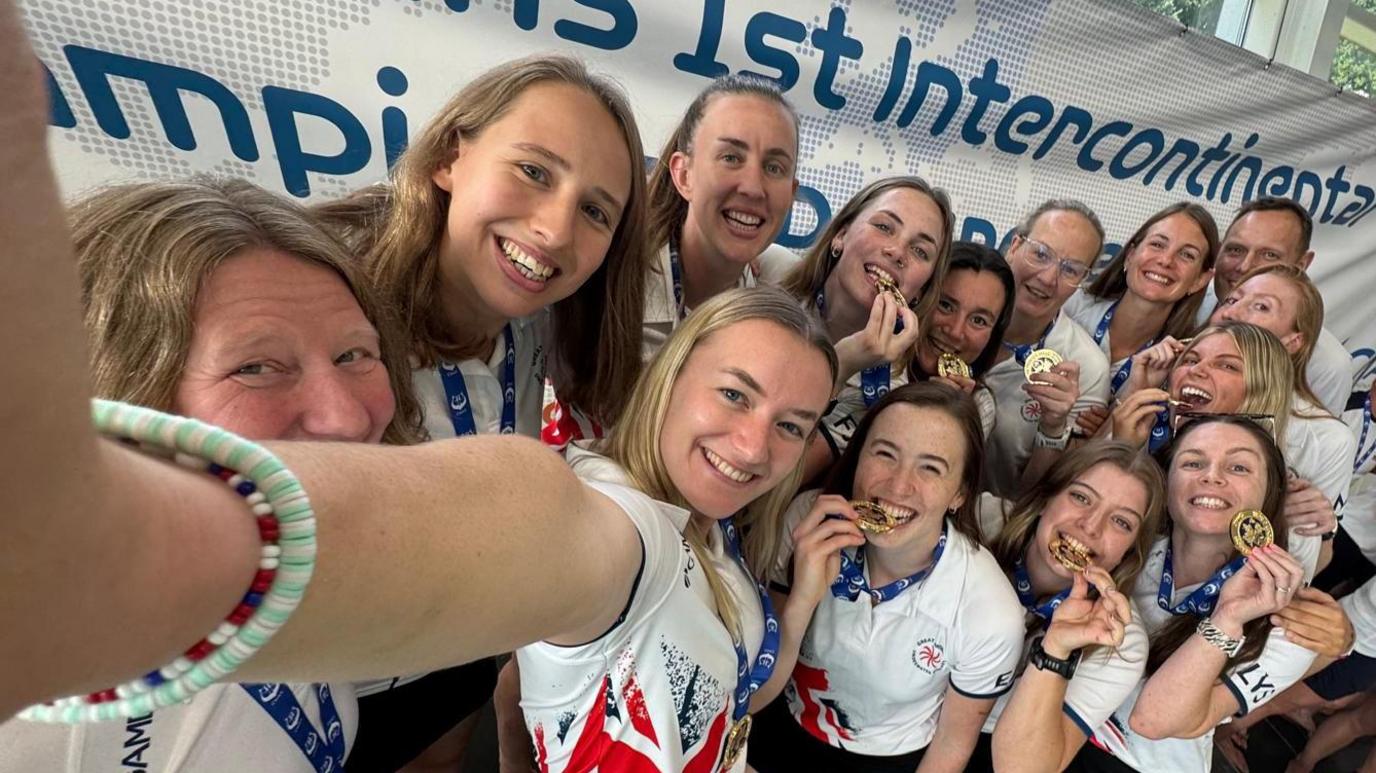 A group of smiling women brandishing gold medals.