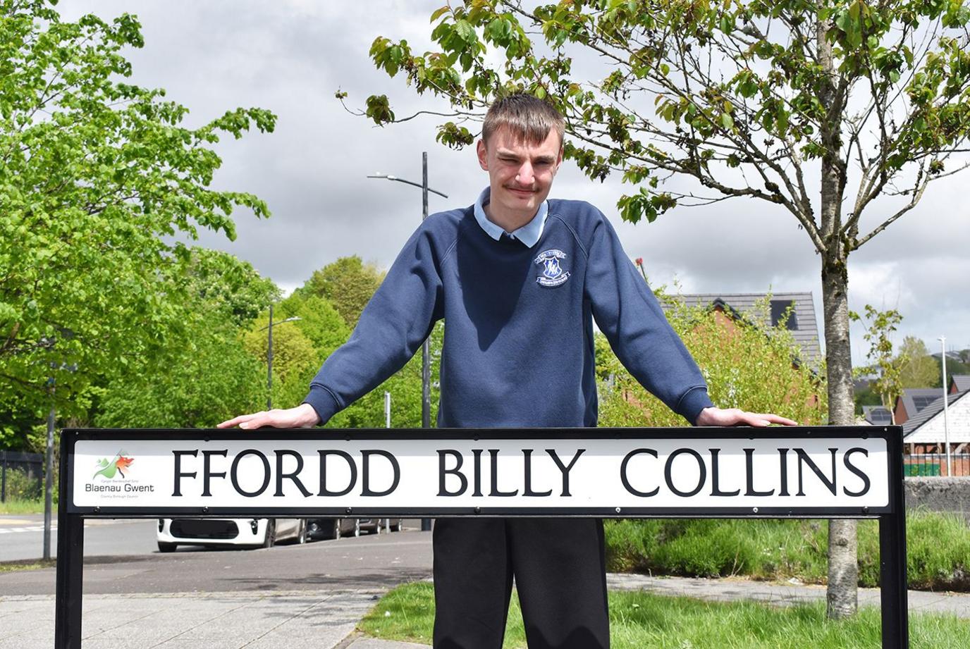 Ciaran Mitchel-Neal standing with a Ffordd Billy Collins sign