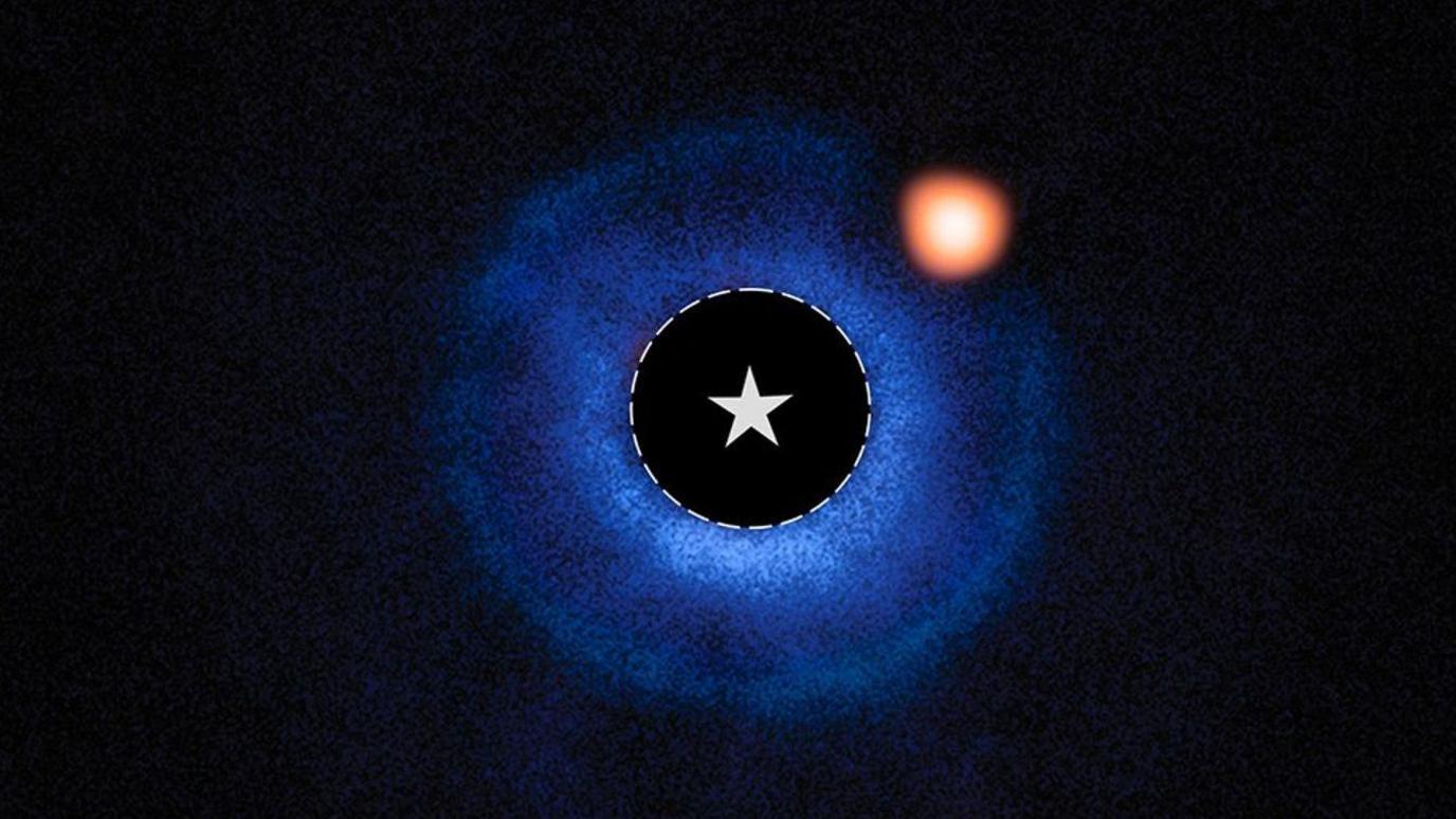 An image of a nearby star and its vicinity. The star symbol at the centre of the image marks the star’s location. A fuzzy blue disc surrounds the star. An orange spot, near to the star and inside this disc, is identified as a planet orbiting the star. A fainter orange spot far from the centre marks a distant star.