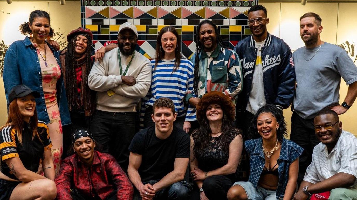 A large group of young musical performers line up in two rows as they face the camera at the Bristol Beacon