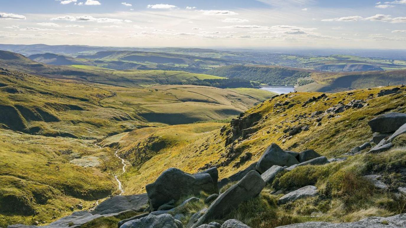 Large rocks on the green slopes and hills of the Peak District on a sunny day.