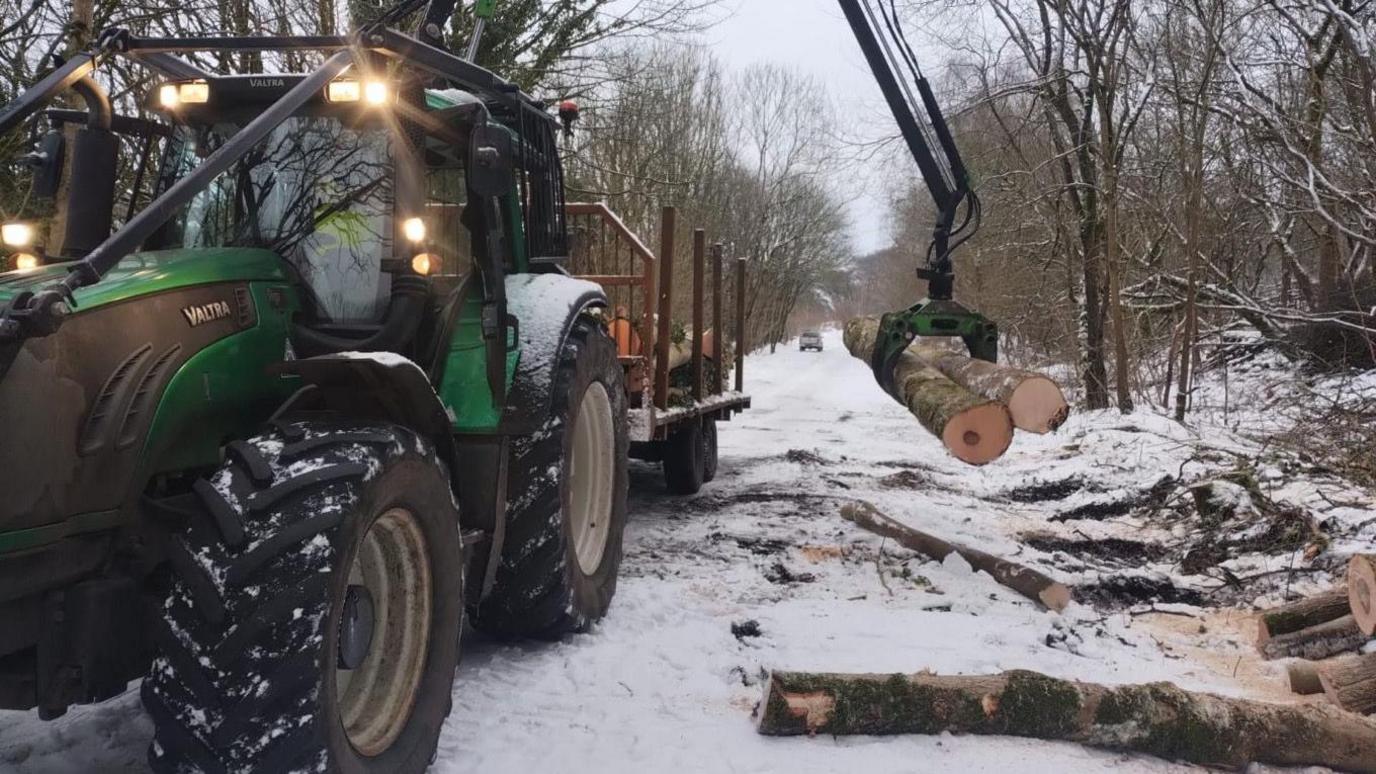 The Monsal Trail covered in snow, with a tractor on it lifting two tree trunks