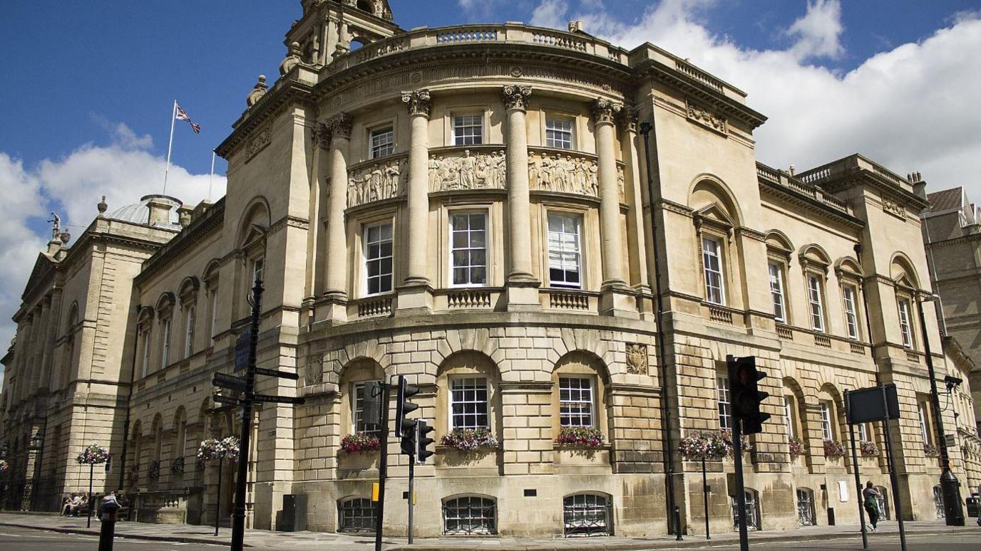 Bath's Guildhall. It is a large brick building on a rounded corner, with stone pillars and tall sash windows.