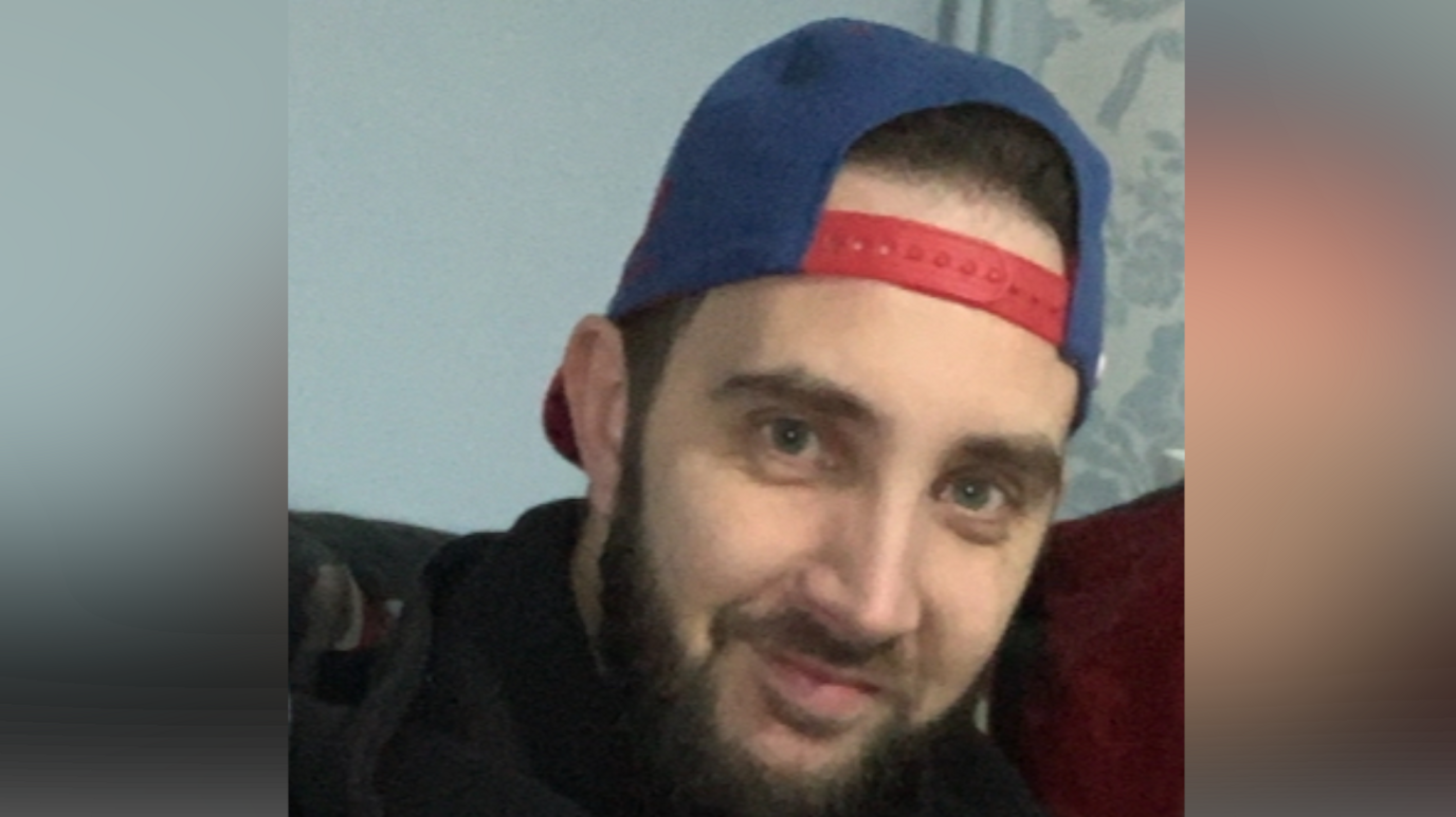 Kevin Doherty wearing a hat backwards on his head. He has dark hair and a dark beard. He is also wearing a black hoodie while smiling at the camera.