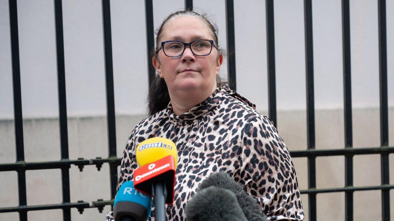 Ch Supt Lindsay Fisherstands outside derry courthouse. A number of media microphones are in front of her. she is wearing a leopard print top. her balck hair is pulled back and she is wearing glasses.