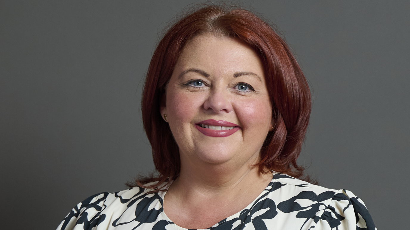 The MP portrait for Paula Barker, who has red hair and is wearing a black and white dress 