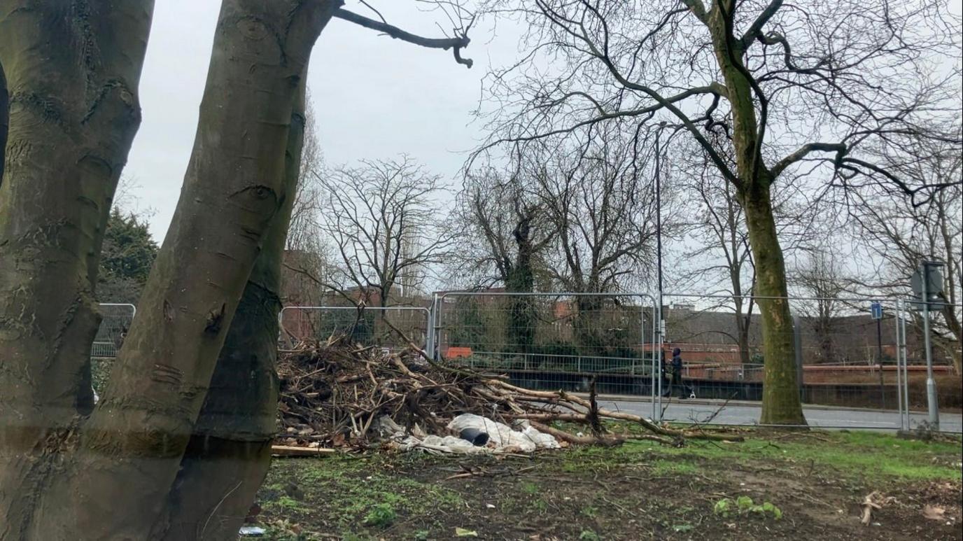 A big pile of rubbish and wood by the metal fence perimeter 