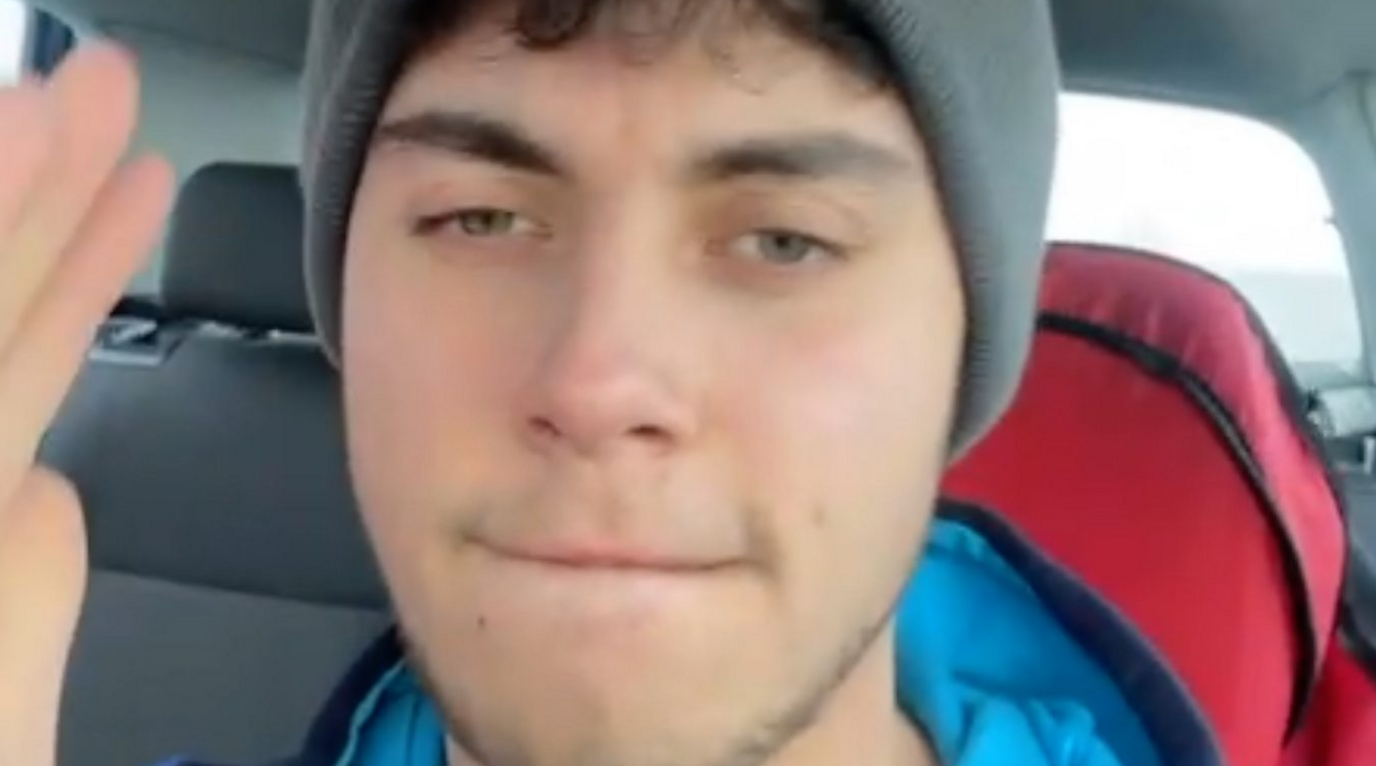 A close-up selfie shot of a young man wearing a grey hat while sitting in a car