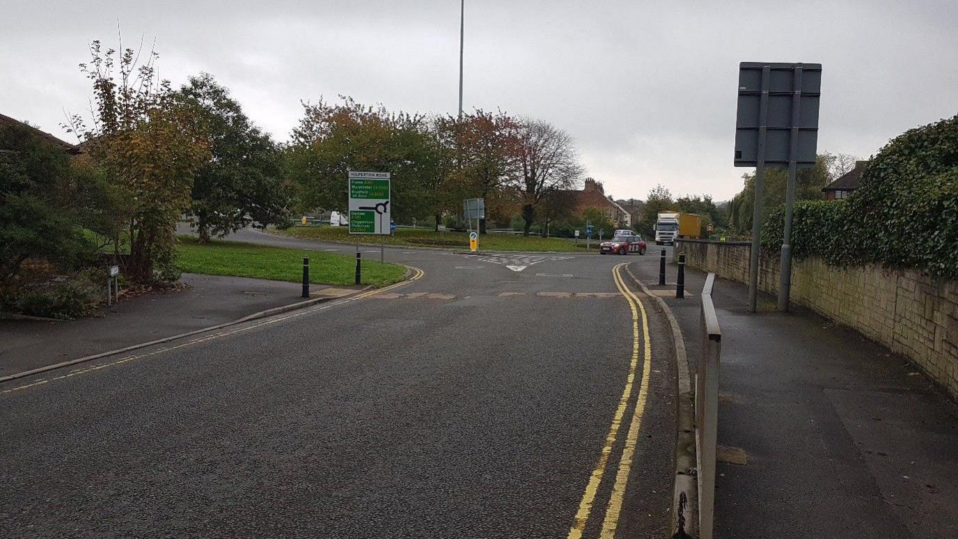 Two cars drive around a roundabout in Trowbridge on a cloudy autumnal day.