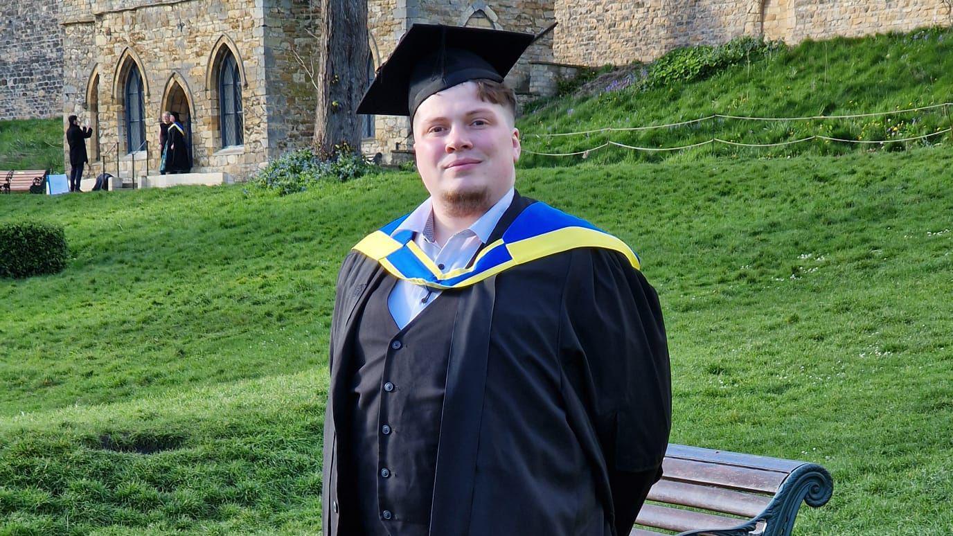 Martin, a brown haired man, poses in his graduation cap and gown