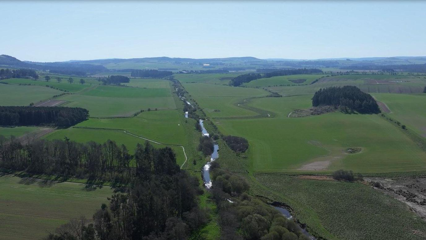 A river running down a straightened bank, surrounded by green farmland and fields.