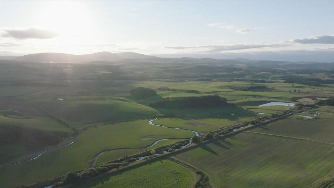 A river in a green fields, which swirls off course into more green fields in a bendy shape.