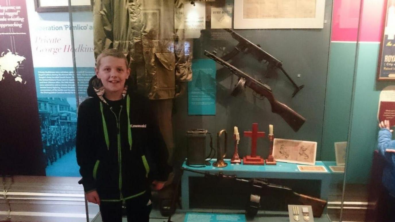 James pictured as a young boy pictured at a museum display of a soldier's uniform and gun.