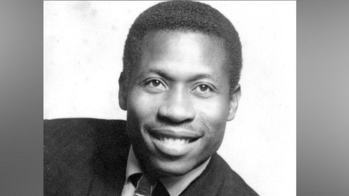 A black and white picture of a black man in a suit smiling at the camera