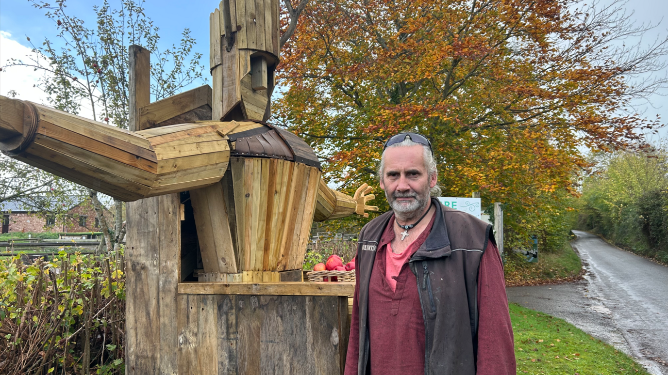 Rob standing beside his Torm Man sculpture standing outside of Torr Cider Farm on an overcast day.