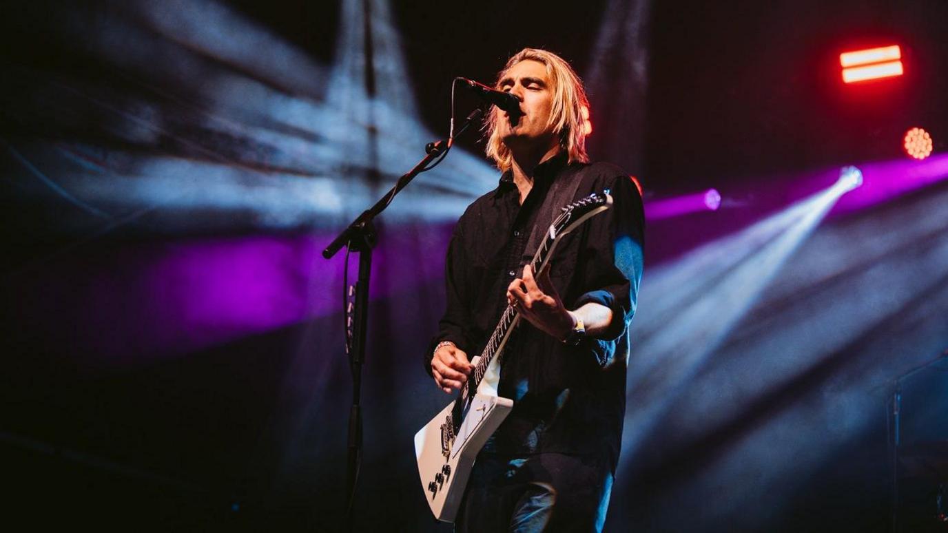 Charlie Simpson of Busted on stage at Bristol Sounds 2024. He is wearing a black shirt and playing a white electric guitar.