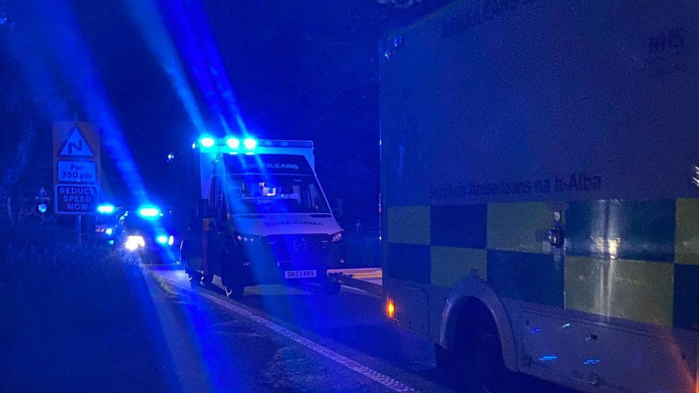 Two ambulances are parked by the road side in the darkness with blue flashing light flashing.