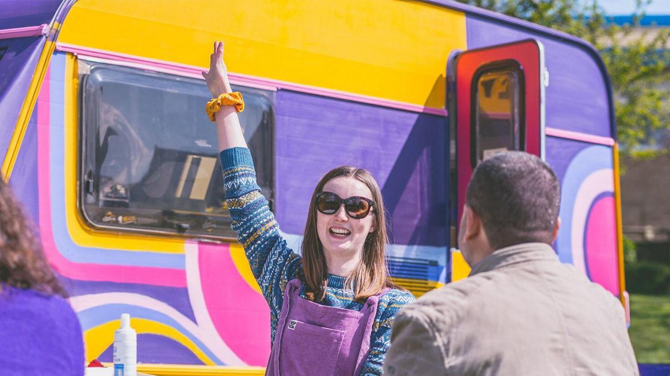 A woman outside a colourful caravan 