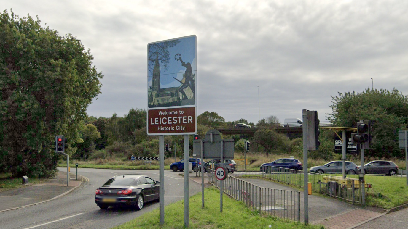 A sign saying "Welcome to Leicester - Historic City, next to a traffic island
