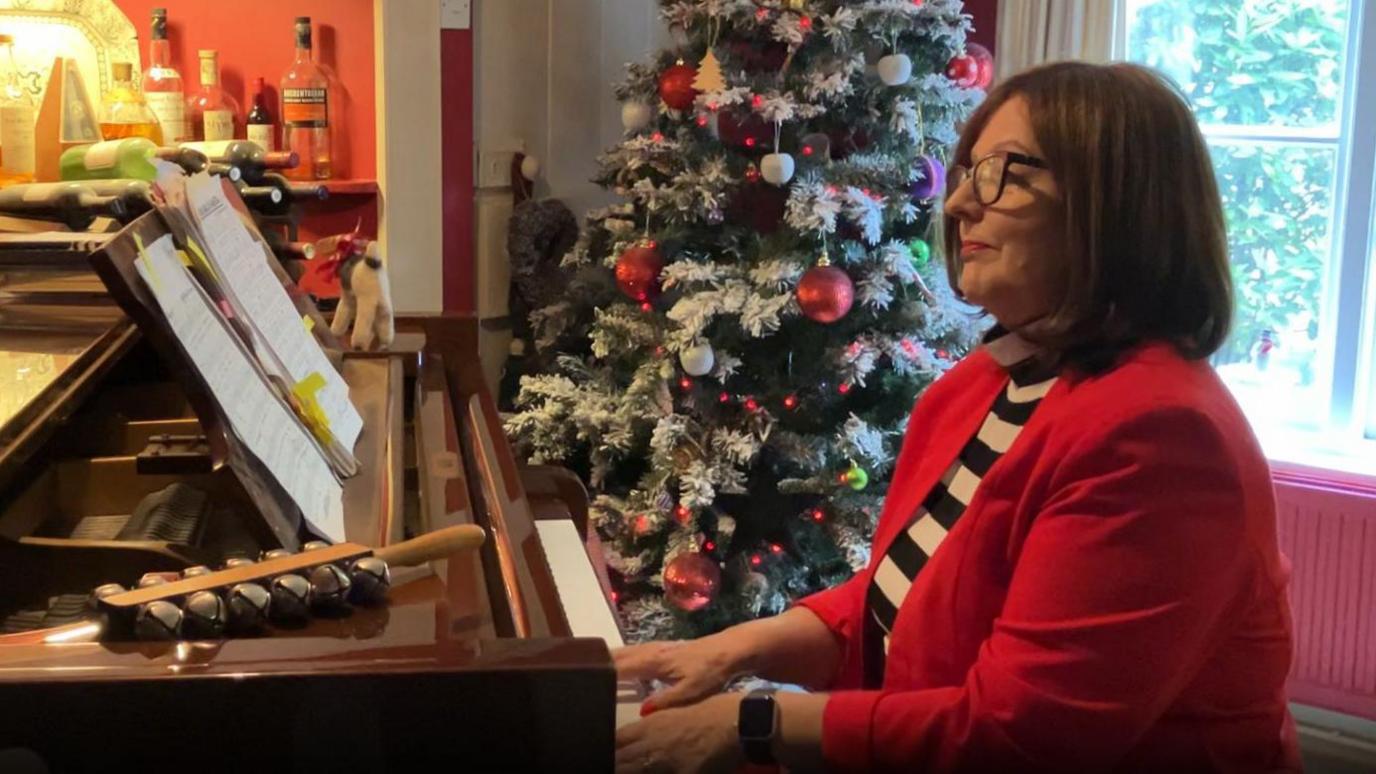 Jane Malyon playing the piano in front of her Christmas tree.