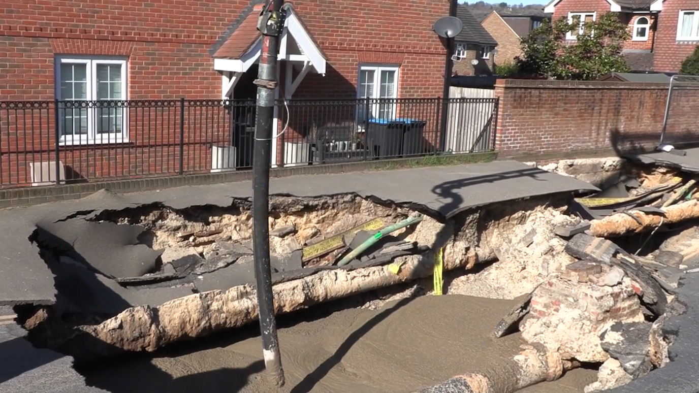 A black pipe putting foam concrete in a large hole in a street.