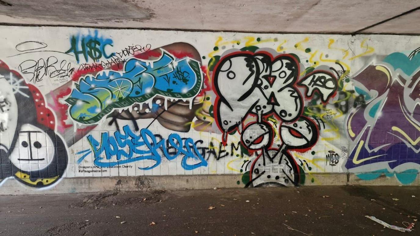 Colourful writing and graffiti painted over an artwork on a white wall.