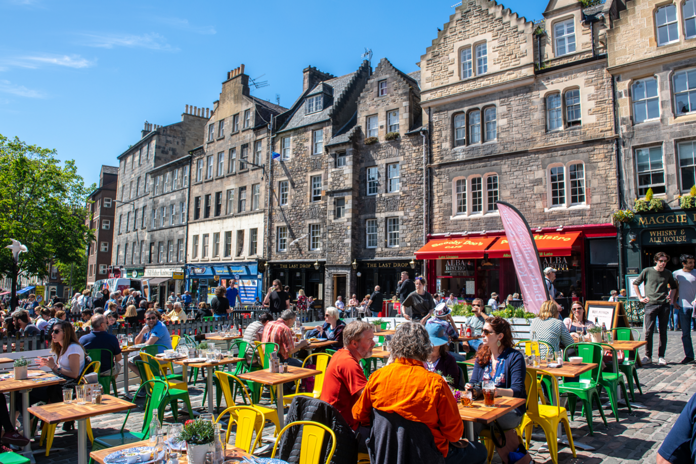 People sitting at colourful tables and chairs in the centre of the Grassmarket.