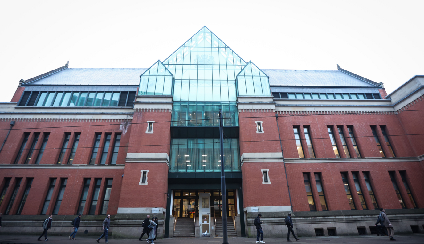 Image shows the exterior of Minshull Street Crown Court in Manchester, a modern building with red brick wall and a bottle-green glass central area above the front area. 