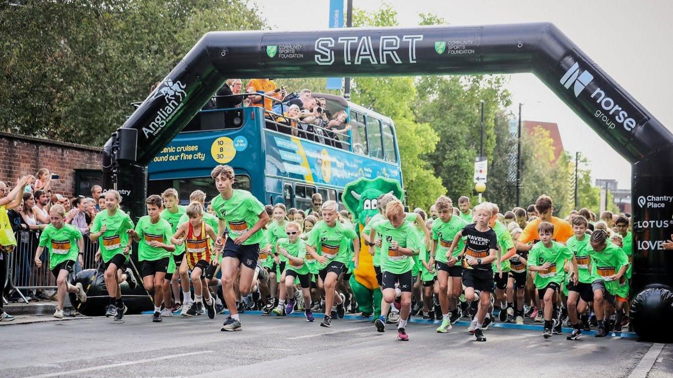 Hundreds of young runners dressed in green t-shirts crossing the start line of Junior Run Norwich