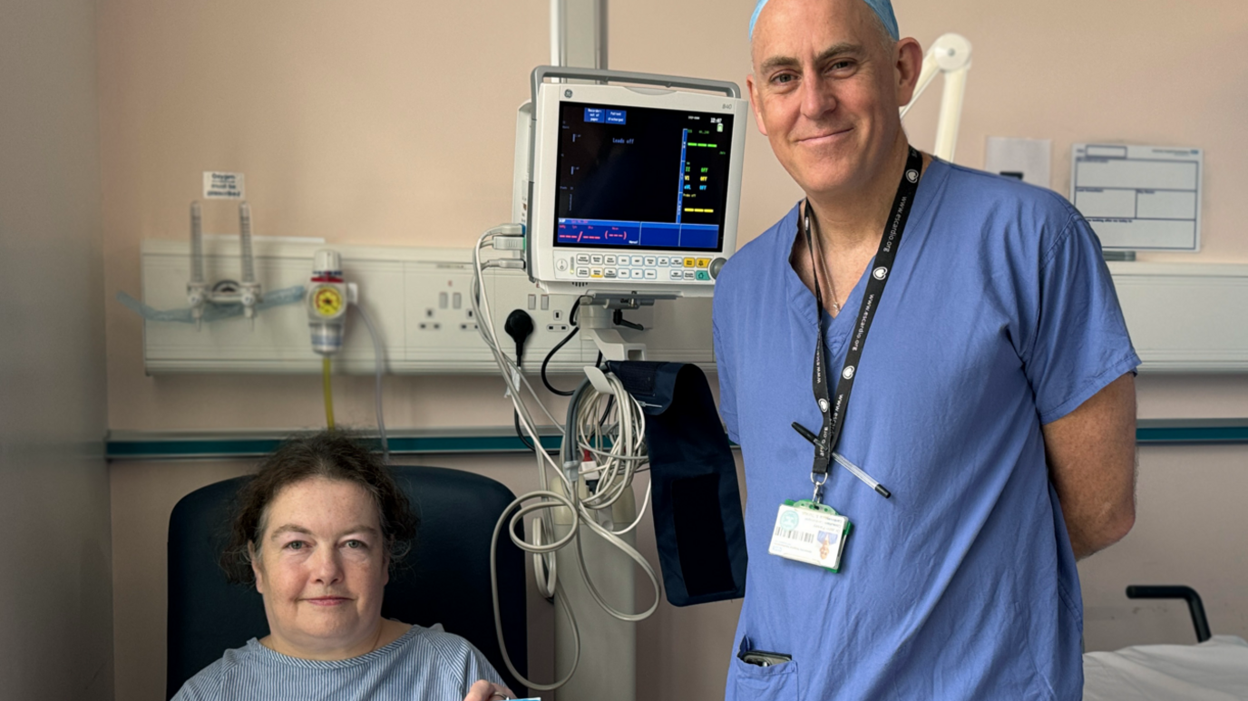 Female patient with a male doctor in a hospital setting with a monitoring screen behind them