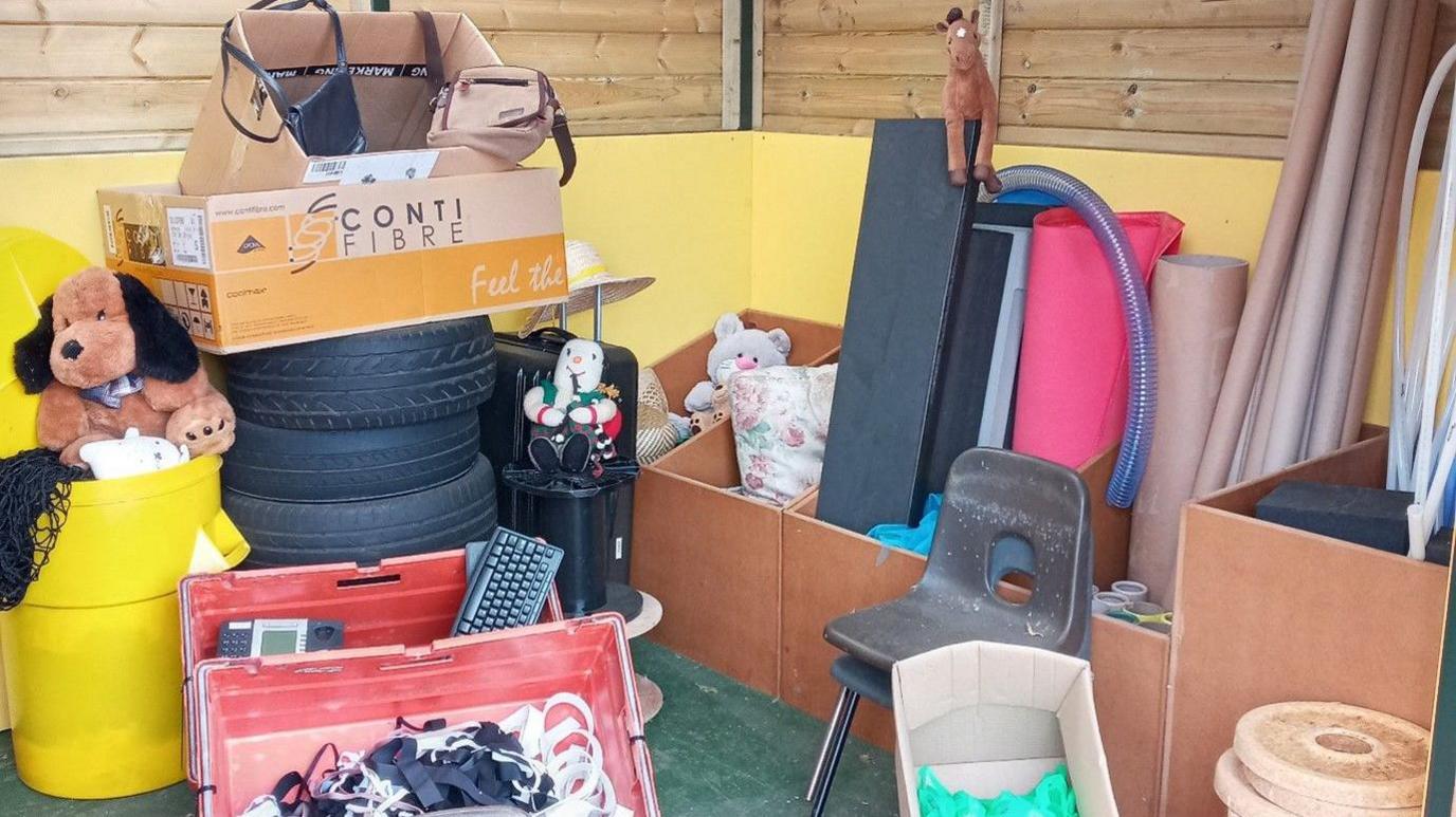 Scrap materials including long cardboard tubes, boxes of material and old chairs, in wooden shed.