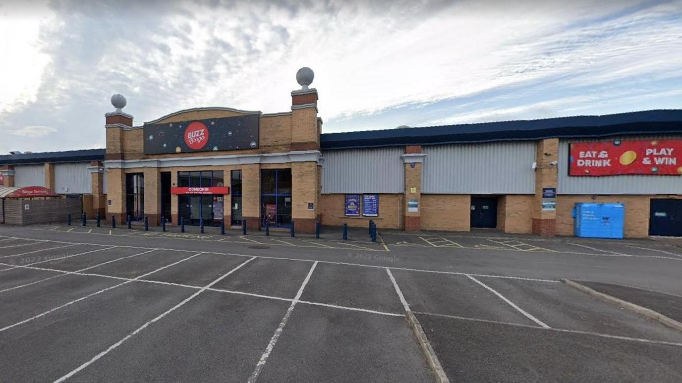 The building is a large warehouse type structure with a large carpark in front of it. You can "East and drink" and "plan and win" according to the sign.