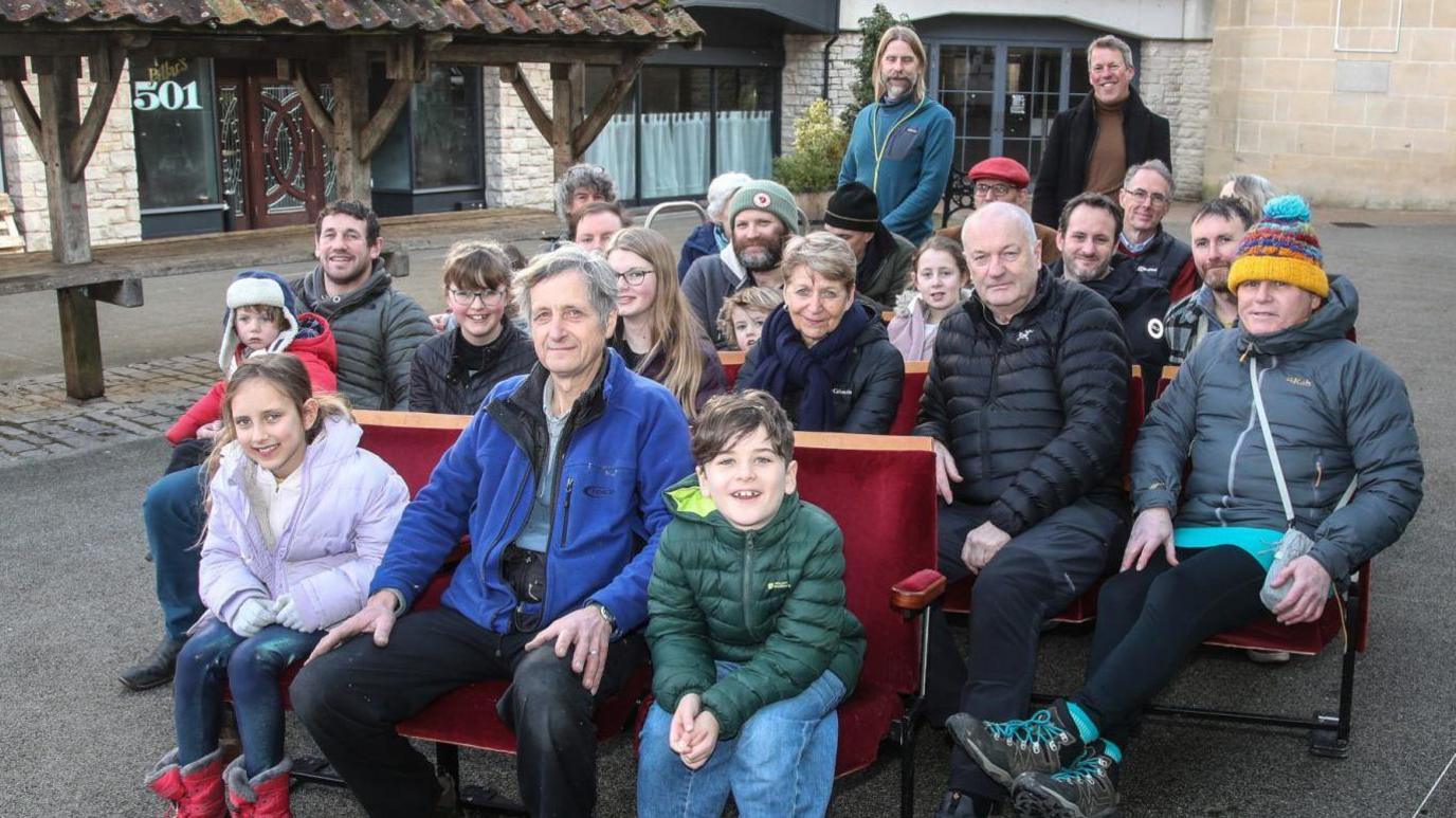 A photo of the campaign group members, including children sitting outside the venue in Shepton Mallet. They are all wearing coats and smiling. 