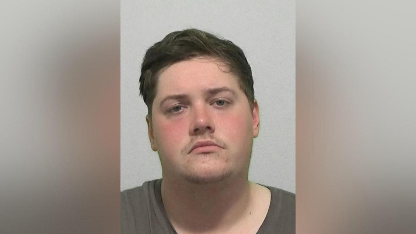 Mugshot of a man with a brown t-shirt and brown hair.