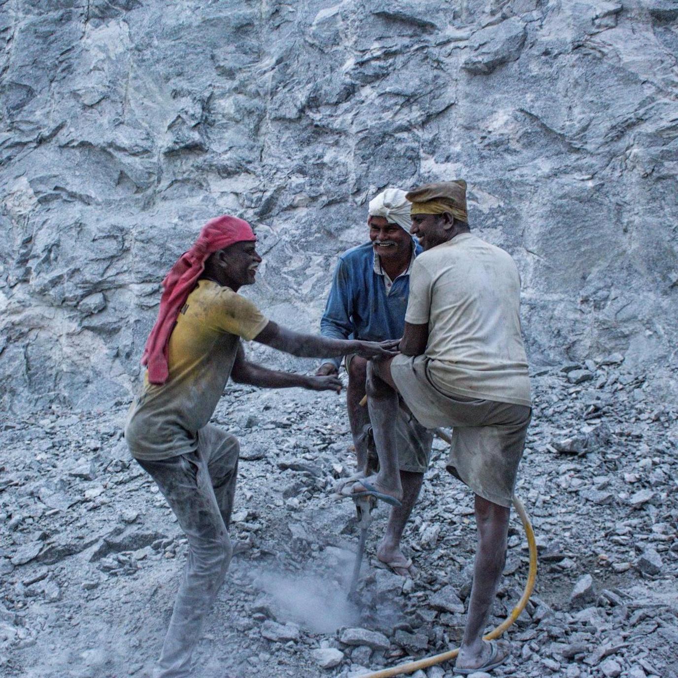 A trio of quarry workers, wearing yellow, blue and white T-shirts, grin at each other and chat as they drill the ground