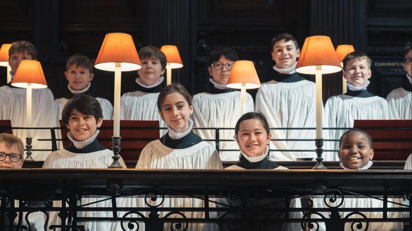 Lila and Lois pose next to the boys in the choir inside in their surplice in inside the cathedral