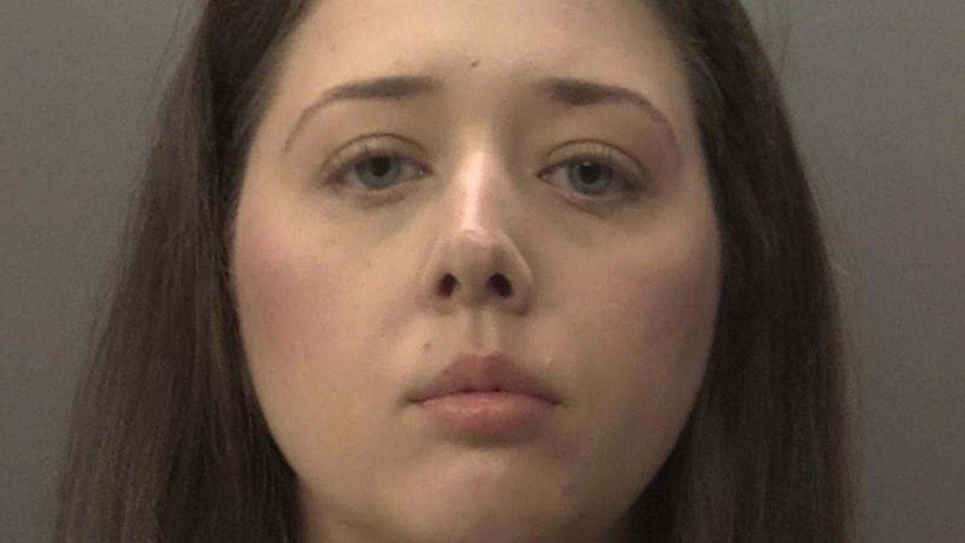 A mugshot of a woman with long brown hair looking at the camera