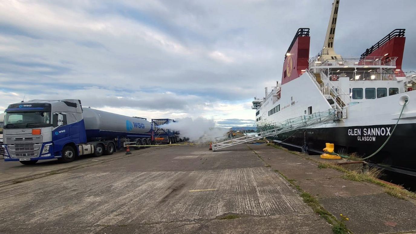 An LNG road tanker is loaded onto Glen Sannox, with a vapour cloud visible