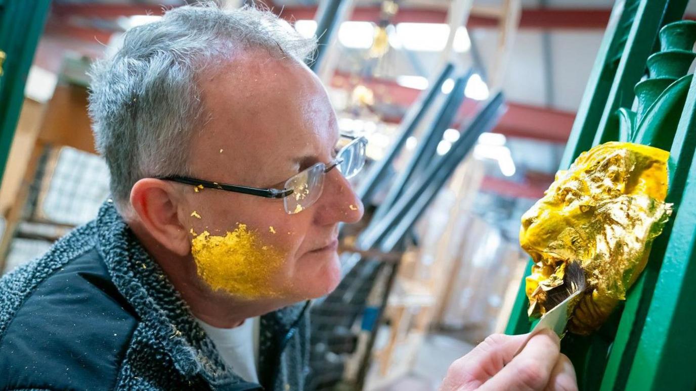 A craftsman applies a final coat of gold leaf paint to the head of a lion on a restored lighting column at Queens Park Bridge, Heywood, Greater Manchester.